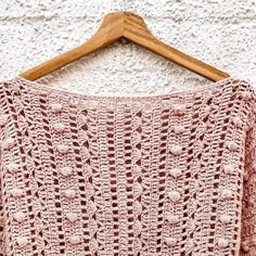 a pink crocheted sweater hanging on a wooden hanger