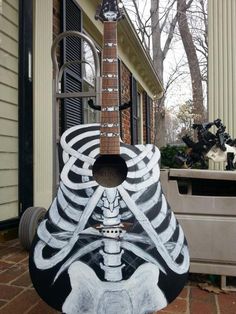 a skeleton guitar sitting on top of a brick floor in front of a house next to a planter