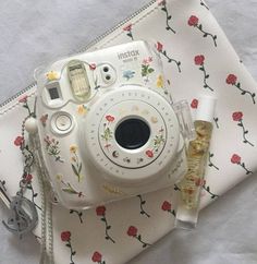 a white camera sitting on top of a table next to a small bottle of perfume