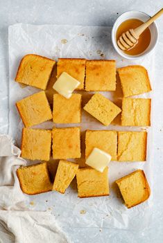 slices of cake with butter on top next to a cup of honey and spoons