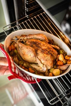 a person holding a roasting pan filled with chicken and vegetables in an oven,