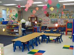 an empty classroom with tables and chairs in the center, colorful decorations hanging from the ceiling