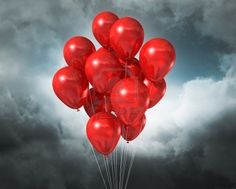 a bunch of red balloons floating in the air on a cloudy day with dark clouds