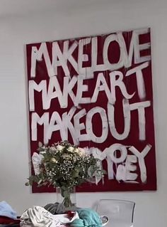 a vase with flowers sitting on top of a table next to a red sign that says make love make art make out try