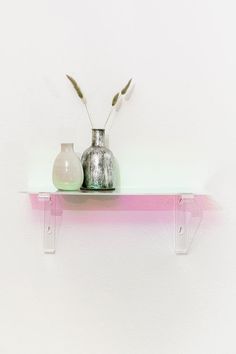 two vases sitting on top of a shelf in front of a white wall with pink and green accents