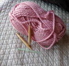 a ball of pink yarn next to two knitting needles