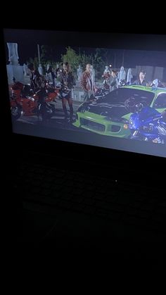 a computer screen with a green car on it and people standing in the dark behind it