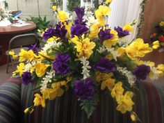 a vase filled with purple and yellow flowers on top of a striped couch next to a table