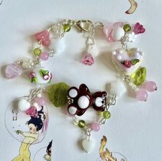 a bracelet with various charms on it sitting on top of a white table next to a cartoon character