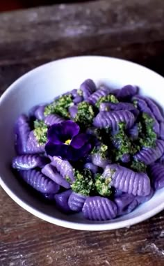 a bowl filled with purple pasta and broccoli on top of a wooden table