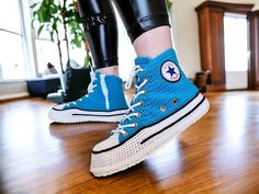 a person wearing blue sneakers and black leggings standing on a hard wood floor