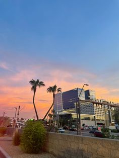 the sun is setting behind some palm trees in front of a large building with many windows