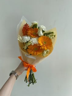 a person holding a bouquet of flowers in their hand with an orange ribbon around it