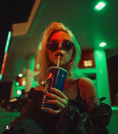 a woman wearing sunglasses and drinking from a blue cup with a straw in her mouth