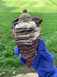 a hand holding an ice cream cone with chocolate and marshmallows on top