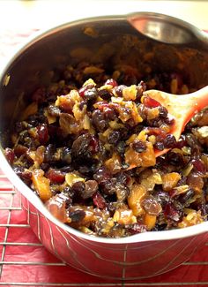 a pan filled with fruit and nuts on top of a red tablecloth next to a wooden spoon