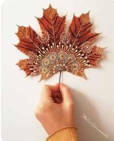 a person holding a fake leaf in front of a white wall with an orange and brown design on it