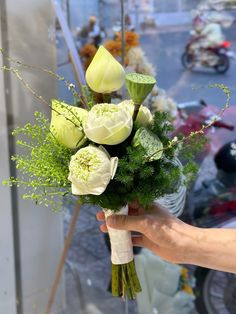 a hand holding a bouquet of flowers in front of a motorcycle parked on the street