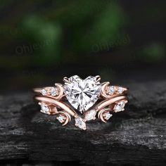 a heart shaped diamond engagement ring on top of a piece of wood with leaves around it