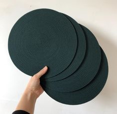 a hand is holding four dark green round placemats on a white background,