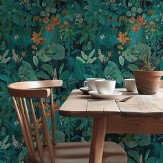 two wooden chairs sitting at a table in front of a wall with plants on it