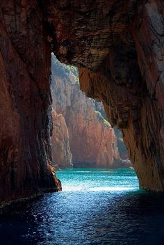 an image of the inside of a cave with blue water and cliffs in the background