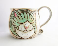 a ceramic mug with a cat's face painted on the front and sides, sitting on a white surface