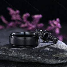 a black diamond ring sitting on top of a rock next to purple lilacs in the background