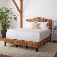 a bed with white sheets and pillows in a room next to a potted plant