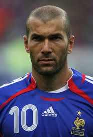 a close up of a soccer player with a bald head and blue jersey on, looking at the camera