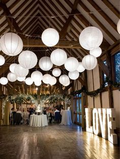 a room filled with lots of white paper lanterns hanging from the ceiling and people sitting at tables