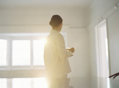 a person standing in a room with sunlight coming through the window and holding a cup