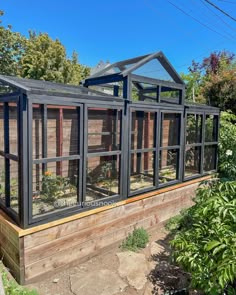 an outdoor greenhouse with several windows on the side and plants growing in the back ground