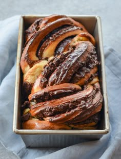 a loaf of bread with chocolate frosting in a baking pan on a blue cloth