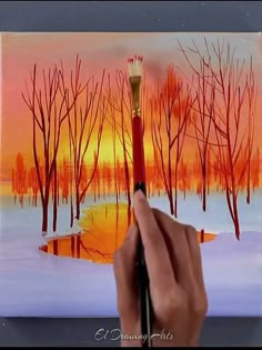 a person is holding a paintbrush in front of a painting with trees on it