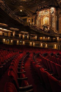 an empty theater with red seats and chandeliers on the ceiling is lit up