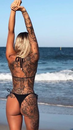 a woman with tattoos on her back standing in front of the ocean