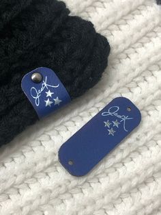 a pair of blue luggage tags sitting on top of a white knitted blanket next to a black hat