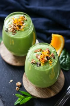 two glasses filled with green smoothie and garnished with orange zeurce