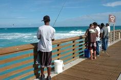 a group of people standing on a pier next to the ocean with fishing rods in their hands