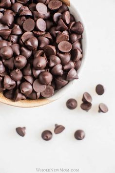 a bowl filled with chocolate chips on top of a white table next to some pieces of chocolate