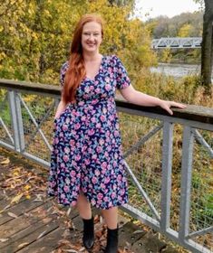 a woman with red hair is standing on a bridge and smiling at the camera while wearing black boots