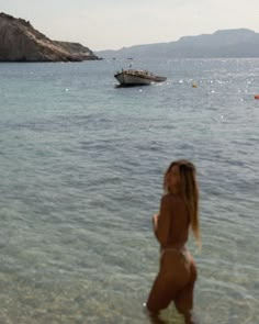 a woman is standing in the water at the beach with a boat in the background