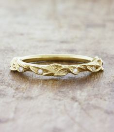 a yellow gold wedding band with leaves and diamonds on the side, sitting on a wooden surface