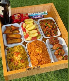 a wooden tray filled with different types of food on top of a grass covered field