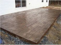 a wooden deck in front of a white house with gravel on the ground next to it