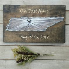 a wooden sign that says our first home and is next to some dried flowers on the table