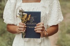 the book of mormon is held by a woman in a white dress and holding flowers