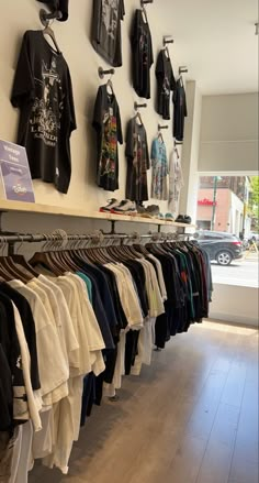 shirts hanging on the wall in a clothing store with wooden flooring and white walls