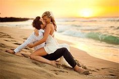 a man and woman sitting on top of a sandy beach next to the ocean at sunset